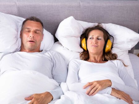 Ein paar liegt im Bett, er schnarcht und Sie trägt einen Gehörschutz