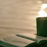 Eine Tasse Tee und ein augeschlagenes Buch auf einem Holzegländer.