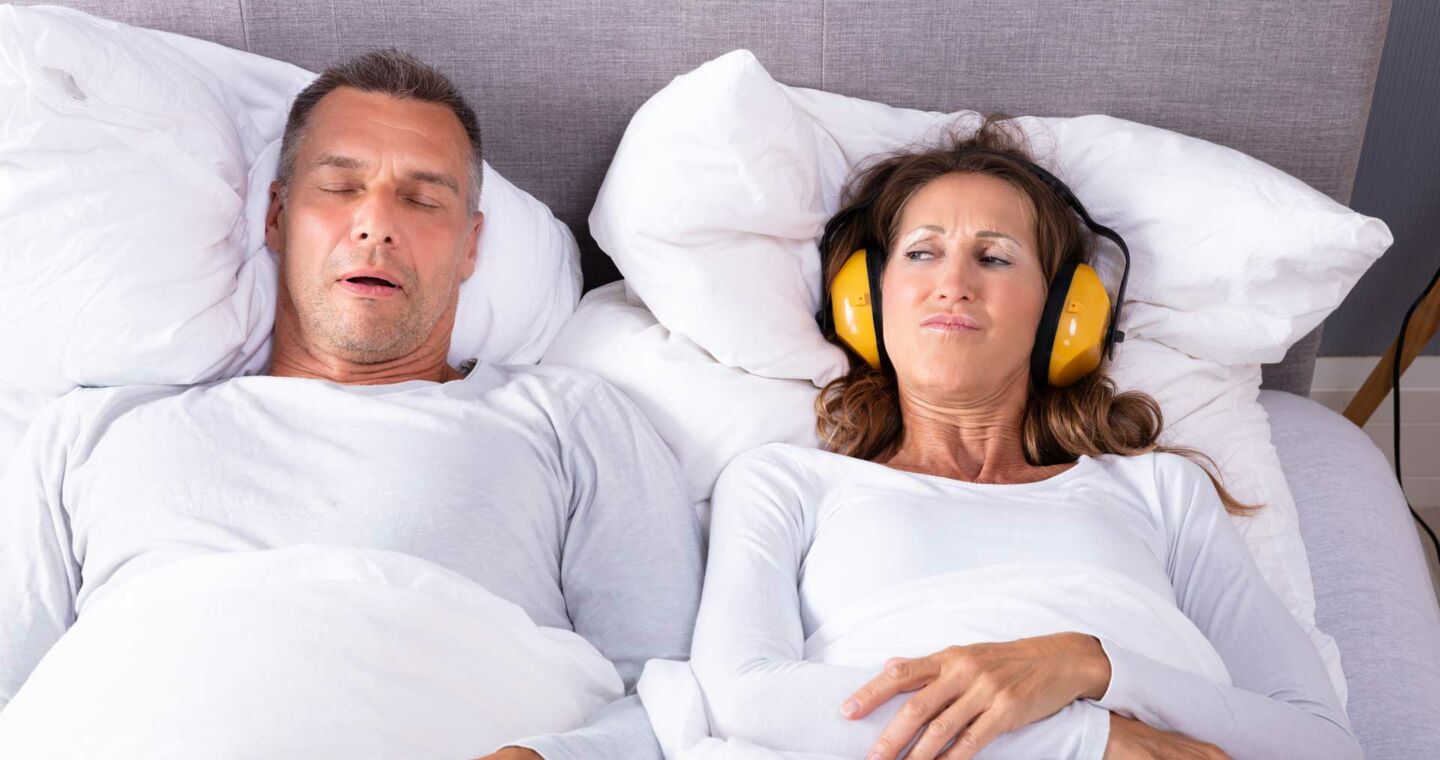 Ein paar liegt im Bett, er schnarcht und Sie trägt einen Gehörschutz