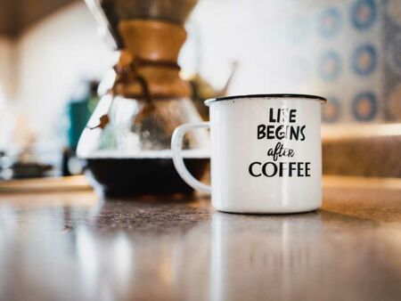 Beschriftete Emaille-Tasse neben einer Kanne mit frisch gebrühtem Kaffee